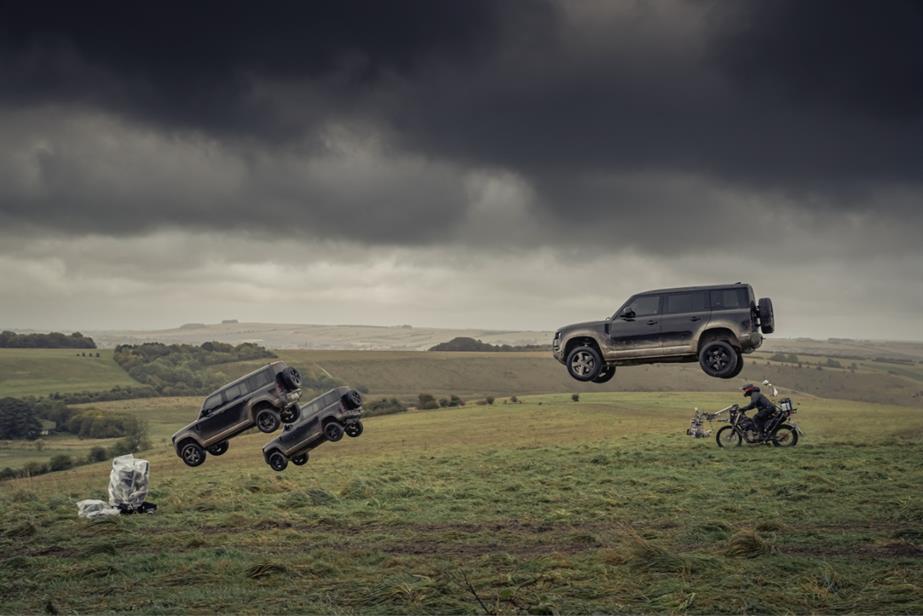 Three Land Rover cars flying through a field
