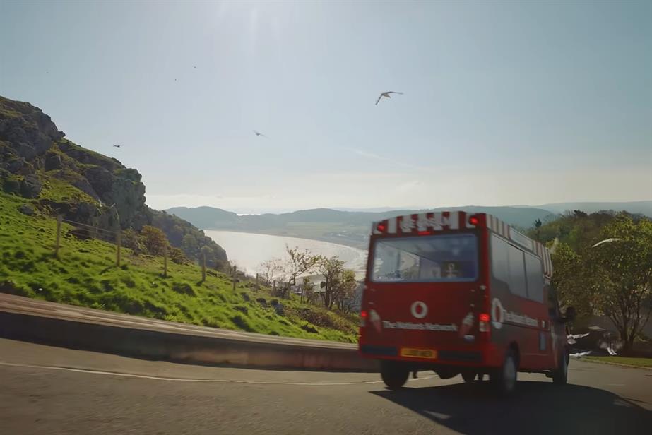 A Vodafone branded van drives down a hill.